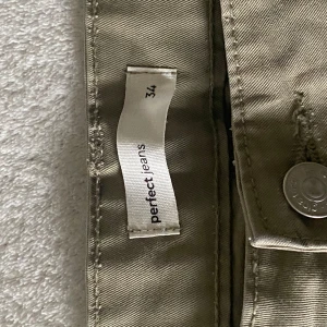 Beiga cargopants från Perfect Jeans - Säljer ett par beiga cargopants från Perfect Jeans i storlek 34. Byxorna har flera stora fickor på benen och bak, klassisk cargostil och är tillverkade i bomull. Perfekta för en avslappnad och trendig look.