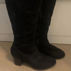 Svarta mockastövlar med klack - Snygga svarta stövlar i mocka med rund tå och stabil klack. Perfekta för att lyfta din outfit med en stilren och klassisk look. Stövlarna har en tidlös design och passar till många olika stilar.