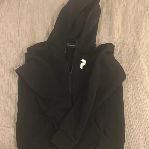 Svart hoodie från Peak Performance S - Tja! Säljer en svart hoodie från Peak Performance med dragkedja och huva. Diskret logga på bröstet och broderad text på ryggen. Mjuk insida och praktiska fickor framtill. Perfekt för chill eller träning. Säljer på grund av att den blivit för liten för mig. Passar 160-168 cm skulle jag säga. Pris kan diskuteras vid snabb affär. Nypris 800 kr 