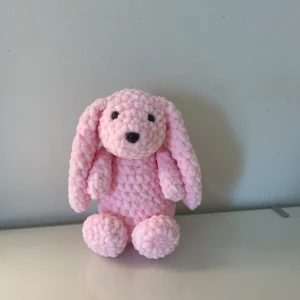 Rosa kanin  - Bilderna visar en rosa, virkad kanin med långa öron och mjuk, fluffig textur. Det är en söt handgjord leksak, perfekt som present eller mysig inredningsdetalj. 