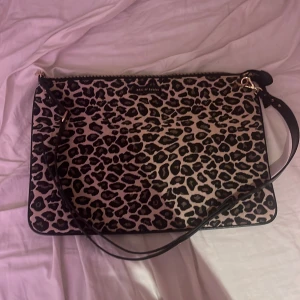 Leopardmönstrad datorväska Ideal of Sweden - Snygg datorväska från Ideal of Sweden med leopardmönster i svart och beige. Väskan har guldfärgade detaljer, dragkedja och justerbar axelrem. Perfekt för att bära din laptop med stil och attityd.