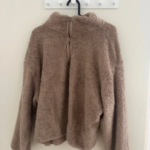 Beige teddytröja med half zip - Supermjuk och fluffig teddytröja i beige med hög krage och half zip-dragkedja framtill. Perfekt för kyliga dagar och har en avslappnad, loose passform med långa ärmar. Tröjan är gjord i mysig fleece och passar perfekt för höst och vinter.