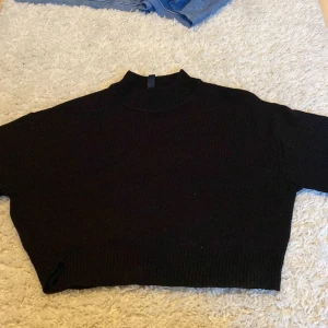 Svart croppad stickad tröja Divided - Svart croppad stickad tröja från Divided med hög hals och korta ärmar. Perfekt för lager-på-lager och passar till både jeans och kjol. Enkel och stilren design som funkar året runt. 40kr med frakt!🚚 