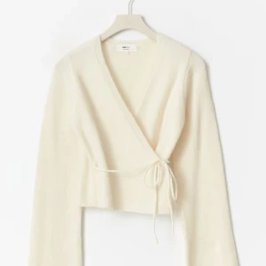 Vit omlottkofta från Gina Tricot - Superfin vit omlottkofta från Gina Tricot med knyt i sidan och v-ringning. Koftan är stickad, har långa ärmar och en croppad passform som ger en trendig look. Perfekt att styla med jeans eller kjol för en clean och fräsch vibe. Relativt ny från juli. Inga defekter, på min bild syns inte snöret som ska gå runt om för att snöret ligger i. Den finns alltså där råkade bara lägga in den🩷