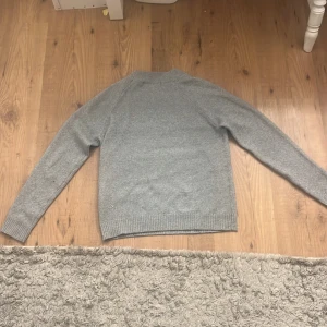 Grå stickad tröja från Vero Moda - En klassisk grå stickad tröja från Vero Moda med rund halsringning och ribbade muddar vid ärmslut och nederkant. Perfekt för lager-på-lager och enkel att matcha med jeans eller kjol. Snygg och basic stil som funkar året runt. Avänd typ 2 gånger men annats i bra skick. Ganska stor i storlek. 