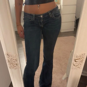 Blå bootcut jeans med broderade fickor - Snygga blå bootcut jeans med låg midja och coola broderade detaljer i guld och silver på bakfickorna. Jeansen har kontrastsömmar och klassisk femficksdesign. Är 170cm och dem sitter bra i längden.