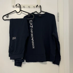 Mörkblå EA7 Emporio Armani sweatshirt - Säljer en mörkblå sweatshirt från EA7 Emporio Armani med vit logga tryckt längs ena sidan framtill. Tröjan har rund halsringning och långa ärmar, tillverkad i mjuk bomull för en skön och avslappnad stil.