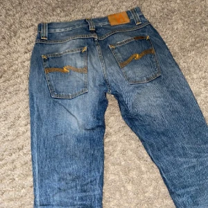 Blå skinny jeans från Nudie Jeans SKRIV FÖR MER BILDER OCH FRÅGOR - Säljer ett par blå skinny jeans från Nudie Jeans med slitna detaljer och klassiska bakfickor med Nudie-söm. Jeansen har normal midja och är tillverkade i stretchig bomullsdenim för en bekväm passform.