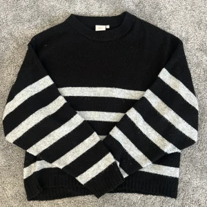 Randig stickad tröja  - Stickad tröja från Nelly i svart med breda vita/grå ränder. Tröjan har en avslappnad passform, rund halsringning och långa ärmar. 