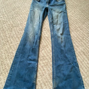 Blå bootcut jeans från Gina Tricot - Snygga blå jeans från Gina Tricot med klassisk bootcut-modell. Jeansen har normal passform och är tillverkade i jeansmaterial med lätt slitna detaljer framtill och baktill. Perfekta för dig som gillar en retroinspirerad look.