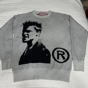 Grå Tyler durden tröja  - Säljer nu en galet snygg grå stickad tröja med svart grafiskt print på Tyler durden från fight club. Tröjan har rund halsringning och långa ärmar. Perfekt för dig som gillar unika och snygga plagg.