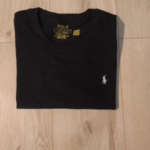 Svart t-shirt Polo Ralph Lauren S - Snygg svart t-shirt från Polo Ralph Lauren med vit broderad logga på bröstet. Modellen är slim fit och har klassisk rund hals. Tillverkad i 100% mjuk bomull, perfekt för en clean och stilren look. Storlek S. Mått: 44 cm över bröstet, 67 cm längd. Helt oanvänd i nytt skick✨