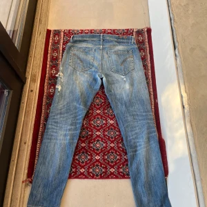 Dondup George ljusblå slitna jeans - Säljer ett par Dondup jeans i ljusblå tvätt med slitningar och hål på benen. Jeansen har klassisk femficksdesign, dragkedjegylf och smal passform. Snygga detaljer på bakfickorna och tydlig faded effekt framtill. Perfekta för en avslappnad streetstil. Pris kan såklart diskuteras!