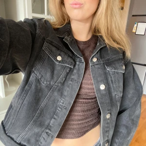 Svart jeansjacka med silvriga knappar - Säljer en svart jeansjacka med klassisk krage och silvriga knappar framtill. Jackan har två bröstfickor med lock och knapp, samt en loose passform som ger en cool och avslappnad vibe. Perfekt att slänga över en t-shirt eller hoodie.