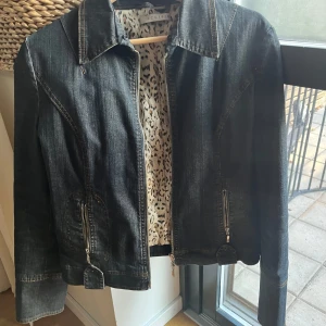 Mörk jeansjacka med leopardfoder - Snygg mörkblå jeansjacka från Acciaio med dragkedja framtill och två fickor med dragkedjor. Insidan har ett coolt leopardmönstrat foder. Säljer då den inte passar min stil och har endast använt fåtal gånger