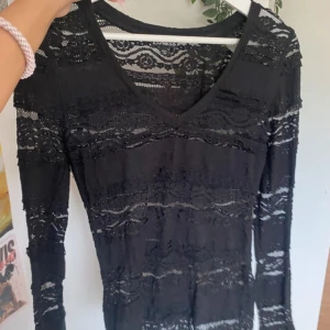 Svart spetsblus  - Säljer en svart långärmad blus från Express i storlek XS. Blusen är helt i spets med v-ringning och genombrutet mönster, vilket ger en snygg och edgy look. Perfekt att styla med jeans eller kjol för en cool outfit.