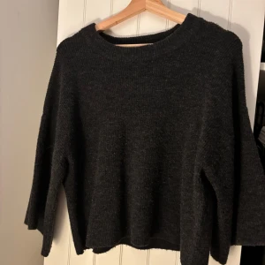 Mörkgrå stickad tröja - Mysig mörkgrå stickad tröja med rund hals och avslappnad passform. Perfekt för kyliga dagar och enkel att matcha med jeans eller kjol. Långa ärmar och mjukt material gör den superbekväm att bära.