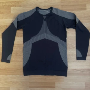 Ny, grå långärmad träningströja - Sportig grå långärmad träningströja från Juritex. Tröjan har coola mönstrade detaljer i grått och är tillverkad i ett stretchigt material av polyamid och elastan. Perfekt för dig som gillar att röra på dig och vill ha en snygg och bekväm look.