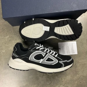 B30 svarta sneakers - Säljer ett par B30 sneakers i svart med vita och grå detaljer. Skorna har en chunky sula, tydlig på sidan och är tillverkade i mesh och syntetmaterial. De har snörning och en sportig vibe som sticker ut. Perfekta för dig som gillar exklusiva och trendiga sneakers.