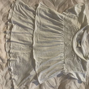 Vit volangtopp med broderad överdel - Supersöt vit volangtopp från Kappahl med broderade blommor på överdelen och volangdetaljer. Perfekt för sommarens alla tillfällen. Lätt och luftig med korta ärmar och rund hals. Extremt trendig och kan användas till alla slags underdelar. Priset kan diskuteras!💕