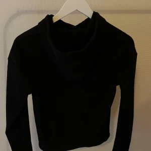 Svart hoodie med lång ärm - En stilren svart hoodie med lång ärm och huva. Tröjan har en klassisk passform och är perfekt för dig som gillar en enkel och clean look. Materialet känns mjukt och bekvämt mot huden.