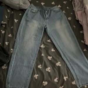 Ljusblå raka jeans med normal passform - Säljer ett par ljusblå jeans med raka ben och klassisk femficksdesign. Jeansen har normal midja och subtila slitningar framtill för en avslappnad look. Perfekta för dig som gillar en enkel och stilren vibe. Materialet är klassisk denim. Har inte haft på mig dom, jag beställde dom men dom va för små och jag kunde inte lämna tillbaka dom så jag har bara provat dom.