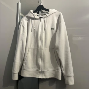 Vit Lacoste zipup - Vit Lacoste zipup med krokodilloggan. Skick 10/10 iprincip helt ny, fick på min födelsedag men använde inte den så mycket. Pris kan diskuteras vid snabb affär.