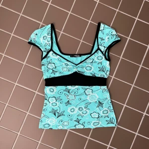 Blommig turkos topp från Jane Norman - Supersöt turkos topp med blommigt mönster från Jane Norman. Toppen har svarta detaljer och knytband i midjan. Storlek s. Använd gärna köp nu🫶🏼