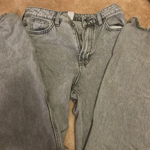 Grå wide jeans från &Denim, strl 34 - Säljer ett par gråa jeans från &Denim i storlek 34. Modellen är wide med ultra hög midja och regular fit. Klassisk femficksdesign och dragkedja i gylfen. Perfekta för dig som gillar en avslappnad och trendig look.