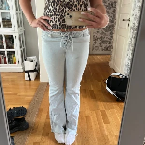 Ljusblå bootcut jeans med snörning - Säljer ett par ljusblå jeans med bootcut och snygg snörning i midjan. Jeansen har klassiska bakfickor och en låg midja som ger en trendig vibe. Märket är stradivarius och de är i storlek 36. Pris kan diskuteras!