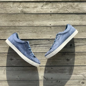 Blå mockasneakers från Timberland - Snygga blå sneakers från Timberland i mjuk mocka med vita sulor och matchande blå snören. Klassisk låg modell med rund tå och diskret logga på sidan. Perfekta för dig som gillar stilrena och bekväma skor med en modern touch.