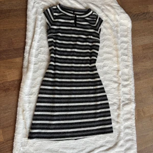 Randig glittrig klänning från Tintoretto - Supersnygg kort klänning från Tintoretto med svarta, grå och vita horisontella ränder och glittriga detaljer. Klänningen har korta ärmar, rund halsringning med liten öppning fram och ledig passform. Perfekt för dig som vill sticka ut med stil! Köpt på el corto englais i Spanien 