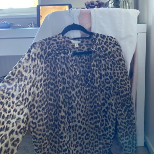 Leopardmönstrad blus från H&M - Säljer en luftig och transparent leopardmönstrad blus från H&M. Skjortan har v-ringning, långa ärmar och är tillverkad i ett lätt, plisserat polyestertyg. Perfekt för dig som vill sticka ut med ett djurmönster och en relaxed vibe.