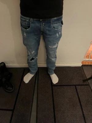 Replay Anbass blå jeans med slitningar - Säljer ett par Replay Anbass jeans i blå tvätt med coola slitningar och detaljer. Jeansen har fem fickor, normal passform och klassisk knappstängning. Materialet är mjukt jeans och de har en snygg faded effekt på låren och bakfickorna. Modellen är 168 cm lång och väger 55 kg. Det är bara att höra av sig vid frågor och funderingar 😀