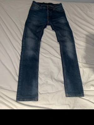 Blå jeans från Nudie Jeans Co - Säljer ett par klassiska blå jeans från Nudie Jeans Co med snygga kontrastsömmar och broderad logga på bakfickan. Modellen har rak passform och normal midja. Materialet är slitstarkt jeans och färgen är mörkblå med ljusare tvättade partier.