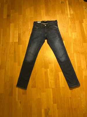Replay Anbass blå jeans herr - Säljer ett par Replay Anbass jeans i klassisk blå tvätt med snygga slitningar och kontrastsömmar. Modellen har fem fickor, normal passform och raka ben. Märkespatch i läder baktill och coola detaljer på bakfickorna. Perfekta till vardagslooken.