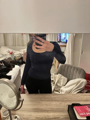 Mörkblå långärmad topp med rund hals - En mörkblå, tight långärmad topp med rundad halsringning. Snygg och enkel modell som passar till många olika outfits. Materialet känns stretchigt och följsamt, perfekt för dig som gillar en slim passform.