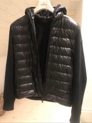 Svart Cardigan från Moncler - Säljer en svart cardigan från Moncler med huva och quiltad framsida. Jackan har dragkedja och är långärmad med slät baksida och ärmar. Perfekt för dig som vill ha en stilren och modern look. BÅDE E-kvitto och vanligt kvitto med följer vid köp samt tags, den är köpt från NK vid göteborg för 12000
