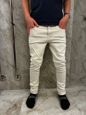 Vita jeans från Polo Ralph Lauren - Säljer ett par vita slim jeans från Polo Ralph Lauren. De har klassisk femficksdesign, smal passform och är tillverkade i ett mjukt bomullstyg. Snygga detaljer med nitar och Polo-logga på fickan. Perfekta för dig som vill ha ett clean och stilrent par jeans.