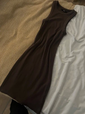 Brun ribbad klänning från Bik Bok - Säljer en brun, ribbad klänning från Bik Bok i storlek S. Klänningen är ärmlös och har en kroppsnära passform med rund halsringning. Materialet är mjukt och stretchigt, perfekt för dig som gillar en enkel och stilren look.