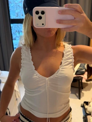 Vit ribbad linnetopp med snörning - Säljer en vit linnetopp med ribbad struktur och snygga volangdetaljer längs axelbanden. 