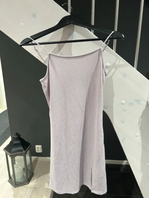 Ljuslila kortklänning - Säljer en stilren ljuslila kortklänning med tunna axelband och en liten slits nertill. Klänningen har en enkel och rak passform, perfekt för varma dagar. 