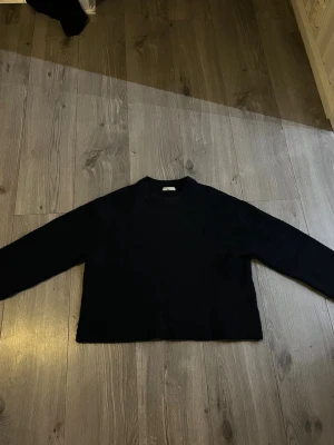 Marinblå stickad tröja med lång ärm - En enkel marinblå stickad tröja med lång ärm och rund hals. Tröjan har en rak passform och är perfekt för lager på lager under kyligare dagar. Passar till det mesta och är ett måste i garderoben.