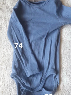 Blå långärmad body - En basic blå långärmad body med rund hals och tryckknappar i grenen. Perfekt för att matcha med andra plagg för små barn.🌸 Fint använt skick. Storlek 74
