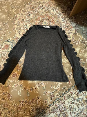 Mörkgrå tröja med volang från Mango - Mörkgrå långärmad tröja från Mango Basics med volangdetaljer längs båda ärmarna. Tröjan har en rund halsringning och är stretchigt.