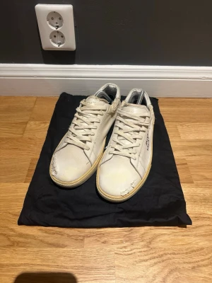 Saint Laurent vita sneakers  - Säljer ett par vita sneakers från Saint Laurent med handskriven logga på sidan. Skorna har slitna detaljer, snörning och beige sula. 