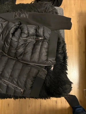 Svart dunväst från Moncler, storlek L - Säljer en svart dunväst från Moncler i storlek L. Västen har quiltad design, flera dragkedjor och ribbade detaljer vid midja och axlar. Insidan har Moncler-logga och en cool serietidningsetikett. Perfekt för dig som vill ha en snygg och varm väst med exklusiv känsla. Dåliga bilder bara o be om nya om ni vill ha 