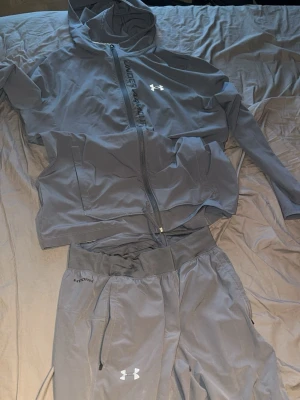 Under armour tracksuit - Bilderna visar ett grått träningsset från Under Armour med jacka och byxor.