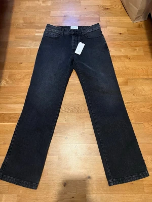 Svarta straight fit jeans från Ami - Säljer ett par svarta jeans i nyskick från Ami Alexandre Mattiussi. Helt oanvända med inga tecken på slitage. Modellen är straight fit med hög midja och raka ben. Jeansen har klassisk femficksdesign, knappgylf och är gjorda i jeansmaterial. Perfekta för dig som gillar en clean och stilren look. 