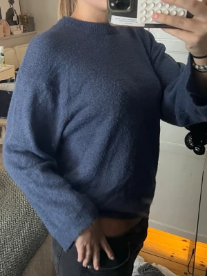 Blå stickad tröja från 157 - Mysig blå stickad tröja från 157 med rund halsringning och avslappnad passform. Tröjan har långa ärmar och ribbade muddar vid ärmslut och nederkant. Perfekt för kyligare dagar och enkel att styla med jeans eller kjol.